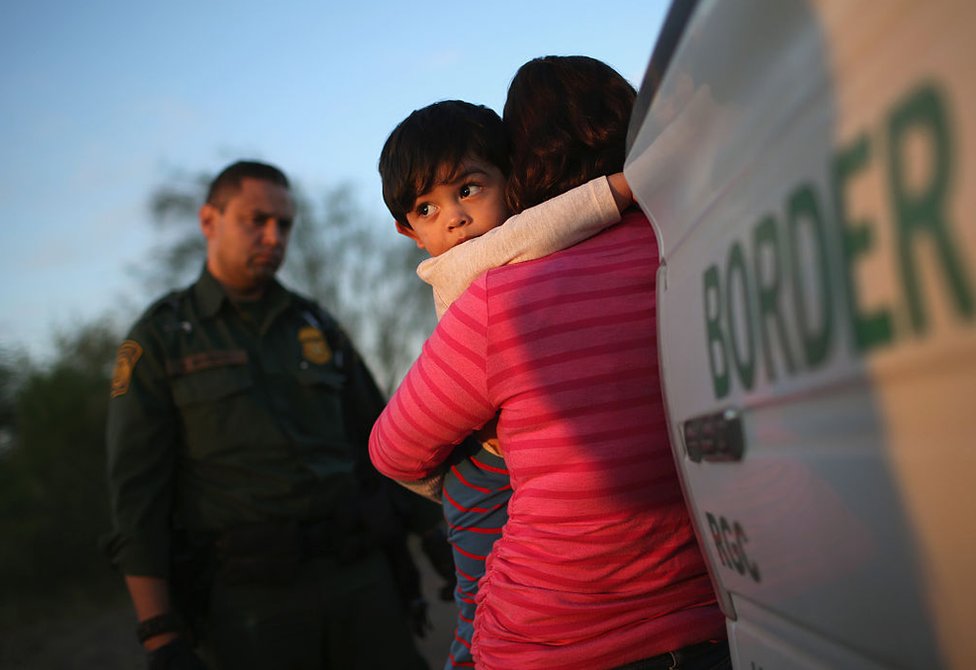 Un niño de un año se agarra al cuello de su madre salvadoreña, quien acaba de cruzar de forma ilegal la frontera entre México y Estados Unidos ante la atenta mirada de un agente de la guardia fronteriza cerca de Río Grande, Texas, el 7 de diciembre de 2015.