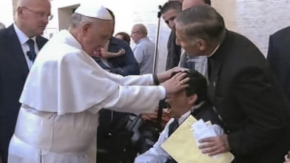 Captura de pantalla de televisión que muestra al papa poniendo sus manos sobre la cabeza de un joven durante una misa de domingo.