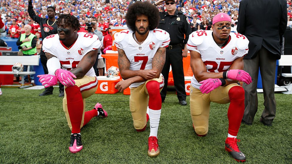 Colin Kaepernick y dos compañeros de rodillas durante la entonación del himno en San Francisco