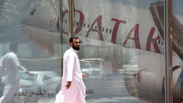 Hombre caminando frente a un reflejo de un avión de la línea aérea de Qatar