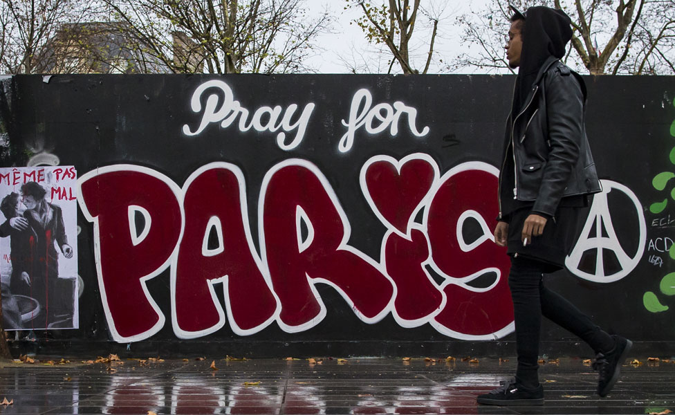A man walking in front of "Pray for Paris" graffiti