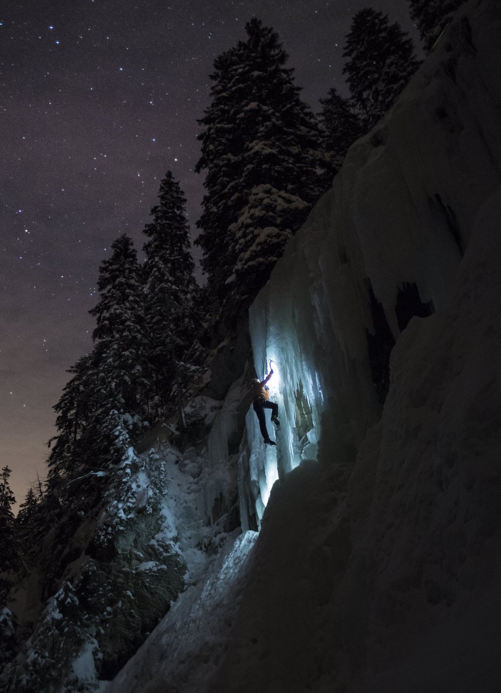 متسلق يصعد في شلال متجمد خلال ليلة مضاءة بالنجوم في مقاطعة فود بسويسرا.