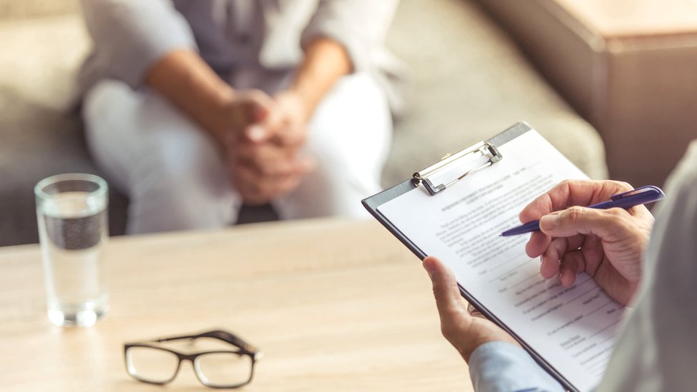 Detalle de libreta de notas y extremidades de doctor y paciente en una consulta.