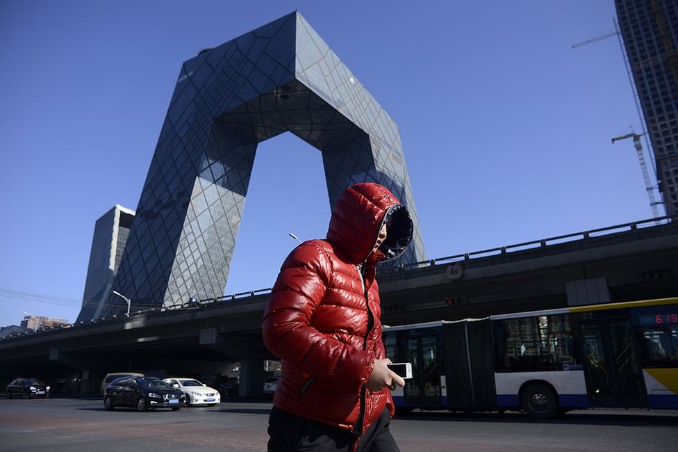 A man walks down the street as the CCTV Tower looms in the background in the central business district in Beijing on 20 January 2017.