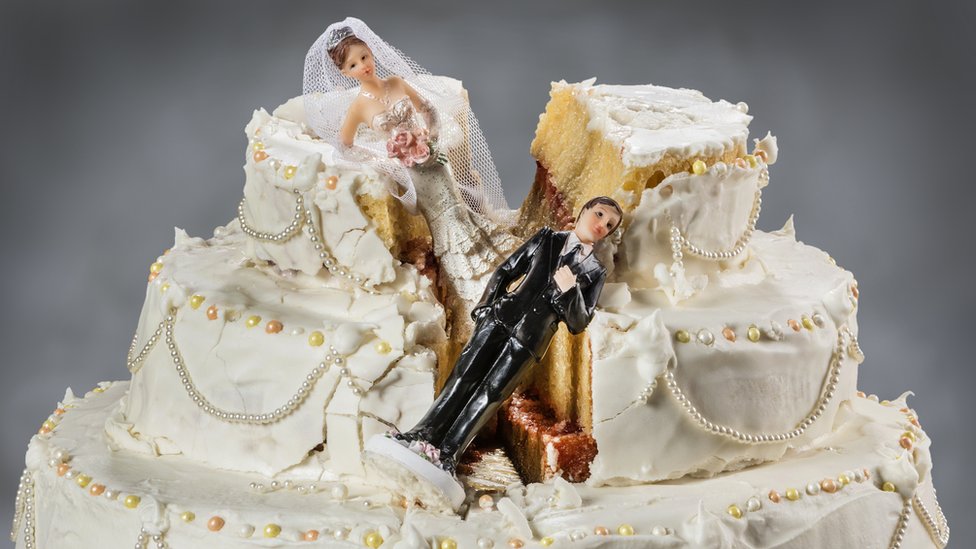 Una torta de boda dividida con las figuras de los novios caídas