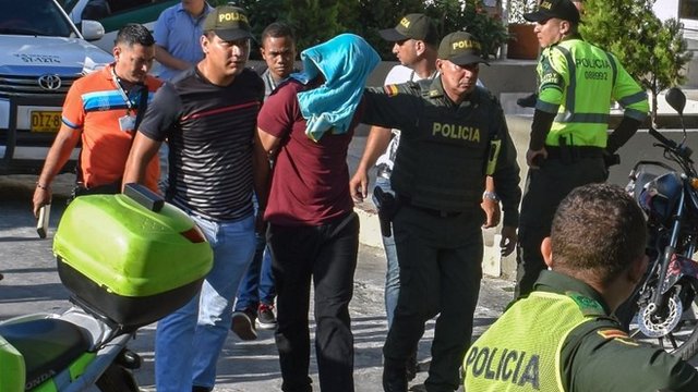 Policía escolta a una persona detenida por su presunta relación con el ataque de Barranquilla.