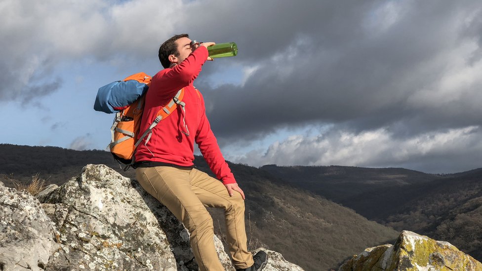 Hombre tomando agua de una botella en una montaña.