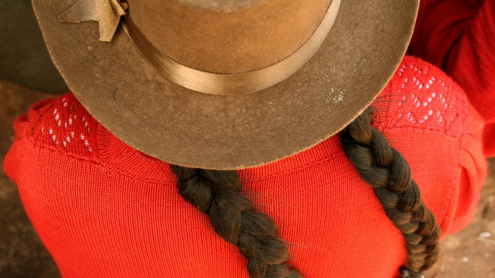Sombrero y trenzas de una mujer peruana con saco naranja