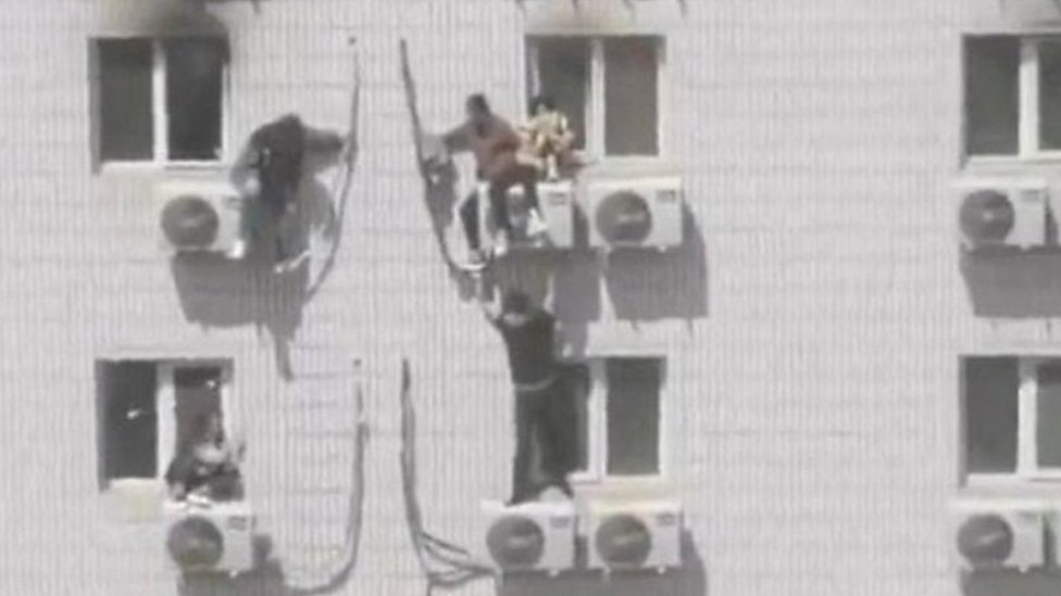 People cling to aircon units on side of burning hospital