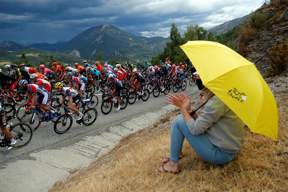 Eine Frau hält einen Regenschirm in der Hand und sieht professionellen Radfahrern beim Vorbeifahren zu