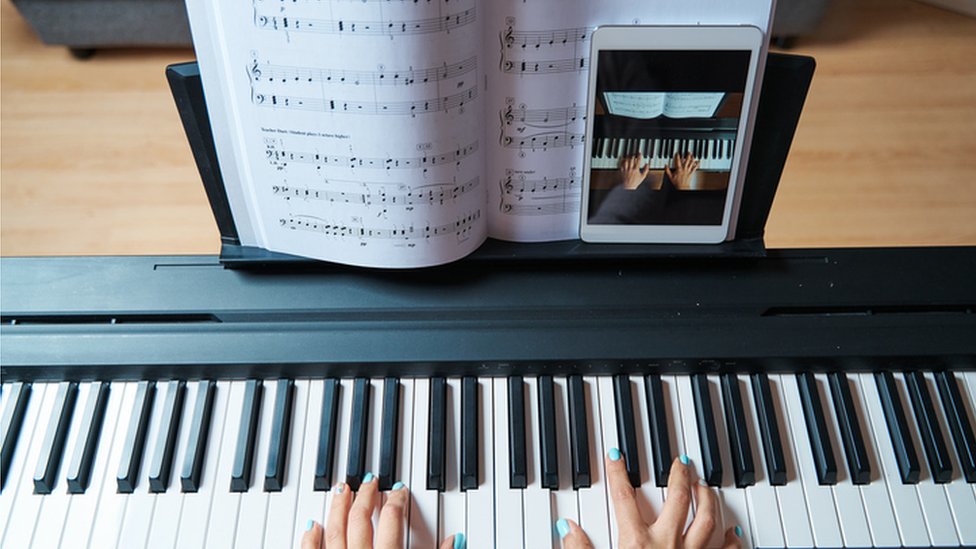 Um homem aprendendo a tocar piano online com um computador em casa