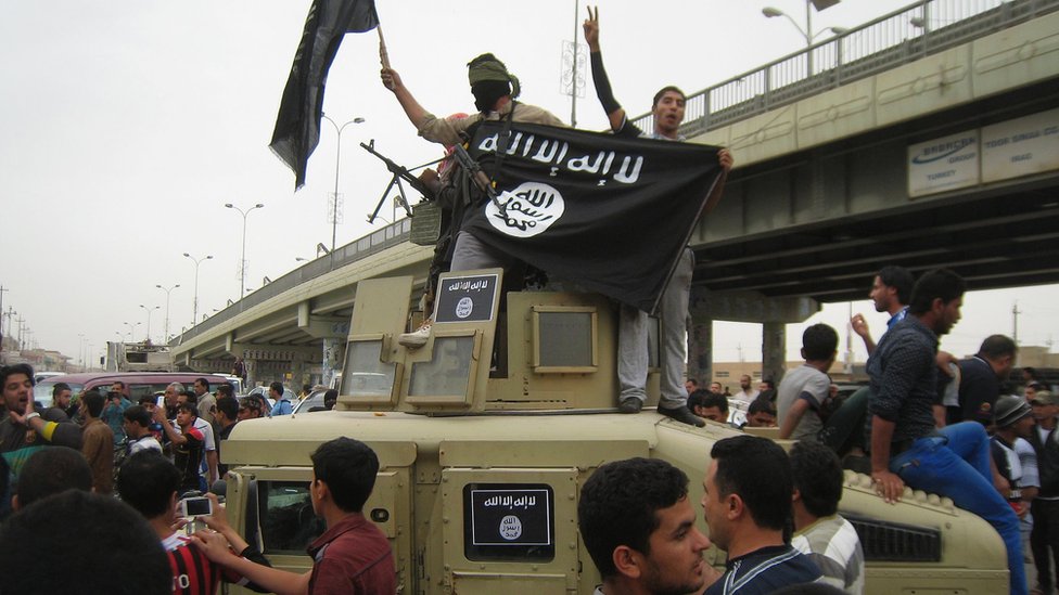 Militantes de Estado Islámico alzan su bandera mientras recorren Faluya en un vehículo militar.