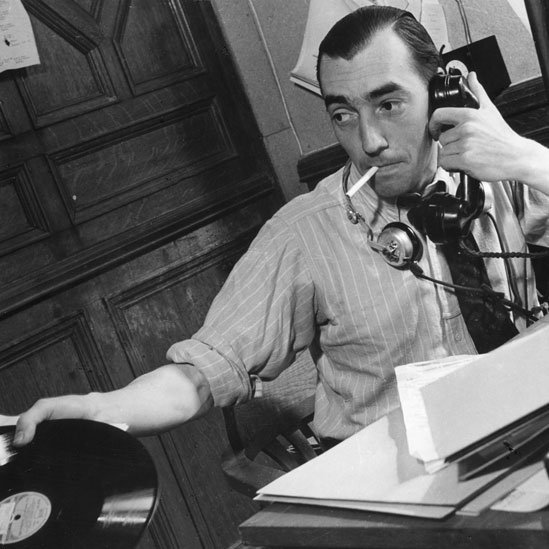 Periodista en el Servicio Latinoamericano hablando por teléfono y con un disco de pasta en la mano, en 1940