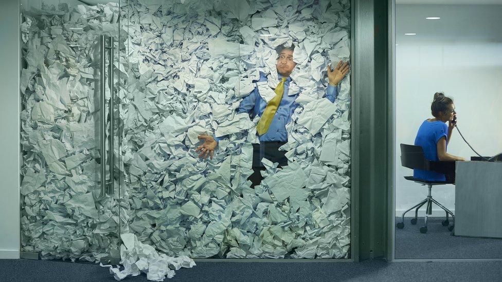 Hombre atrapado en un cubículo lleno de papeles