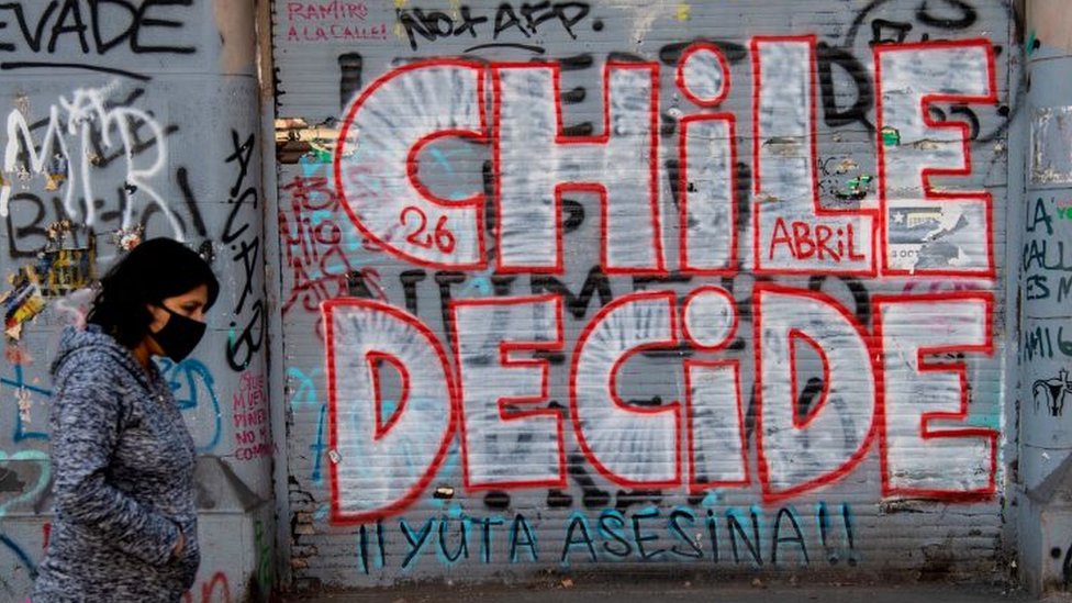 Una mujer camina frente a un grafiti que dice "Chile decide"