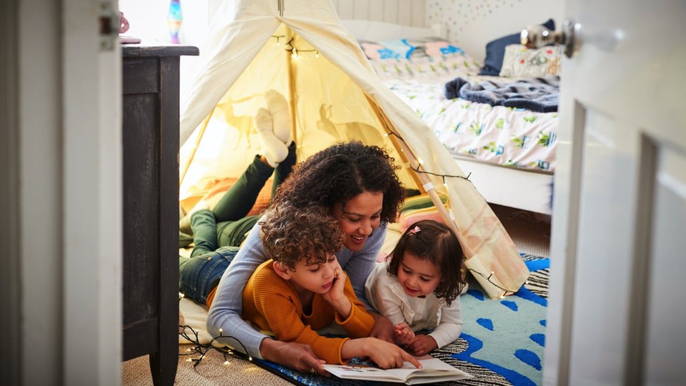 A woman reading a book to her two children under a tent in the bedroom