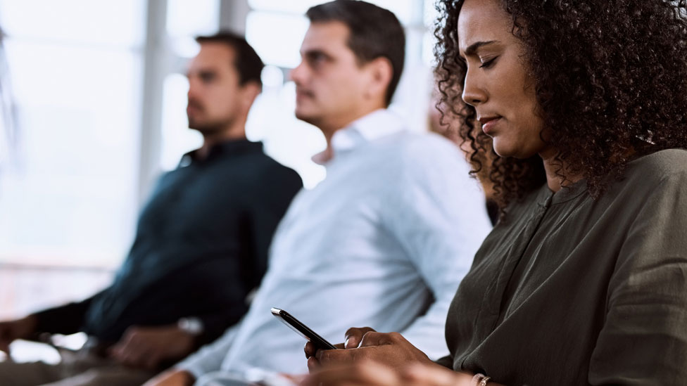 Mulher em uma reunião com o celular em mãos