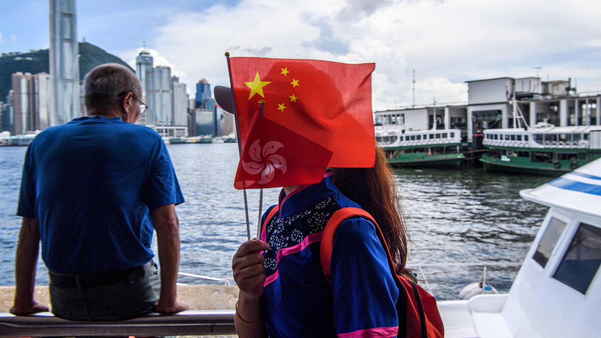 Женщина держит флаг Китая и Гонконга, когда выходит из лодки в гавани Виктория 1 июля 2020 года