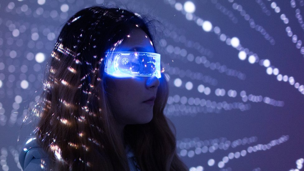 A woman wears augmented reality glasses in a dark room with white dotted lights in the background