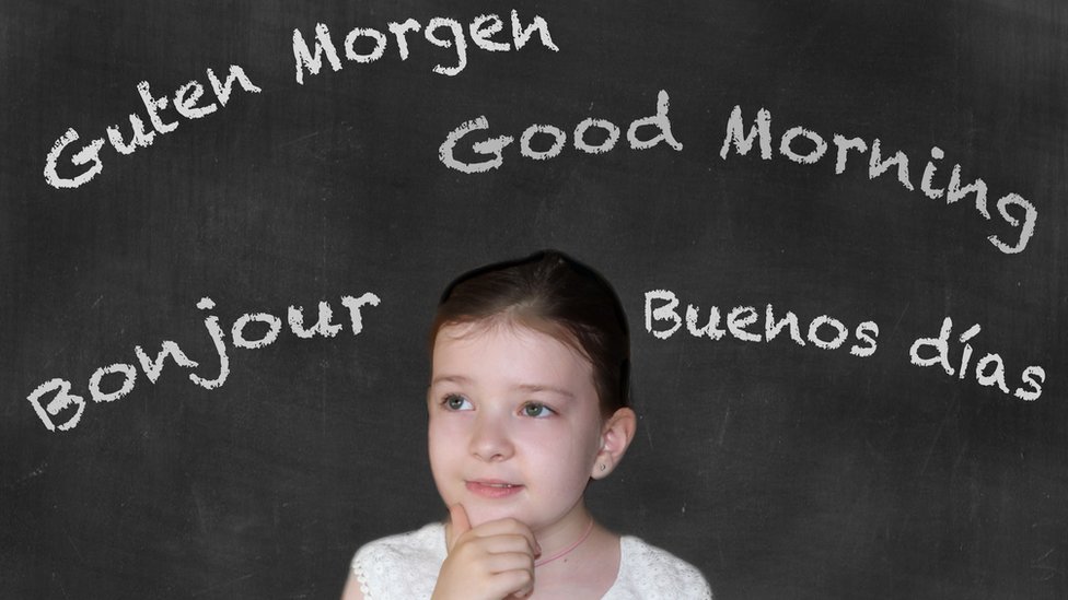 Niña con una pizarra con la palabra buen día en varios idiomas.