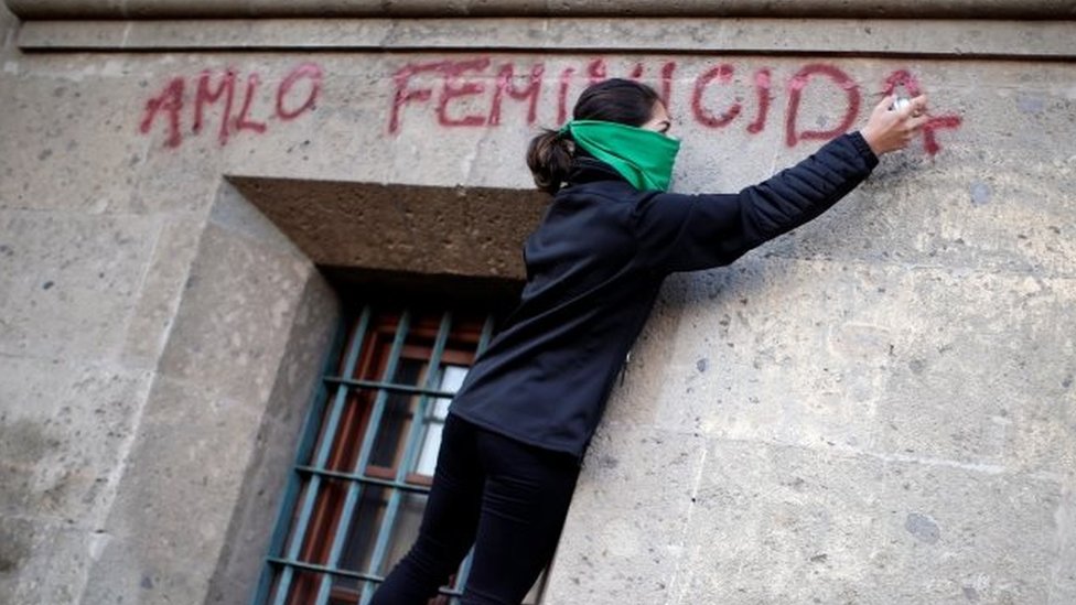 Женщина с баллончиком наносит лозунг с надписью «AMLO женщина-убийца» на стене Национального дворца
