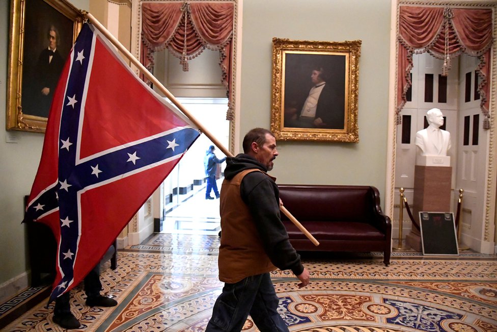 A supporter of President Donald Trump carries a Confederate flag on the second floor of the US Capitol near the entrance to the Senate after breaching security defences, in Washington DC. 6 January 2021.