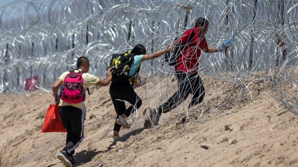 Tres migrantes intentan cruzar la frontera a través de un alambre de púas.