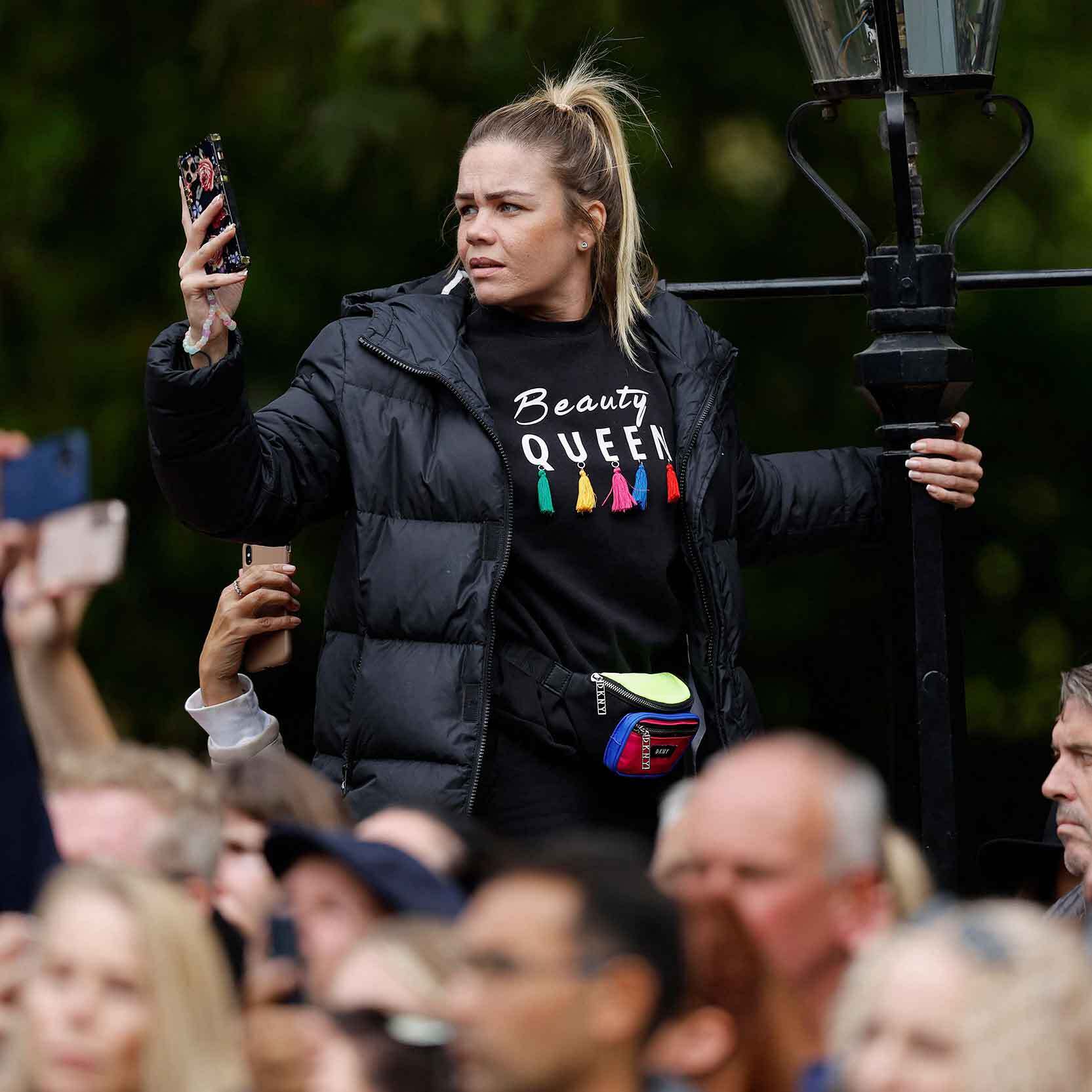 A woman hangs on to a lamppost while trying to take a picture of the procession