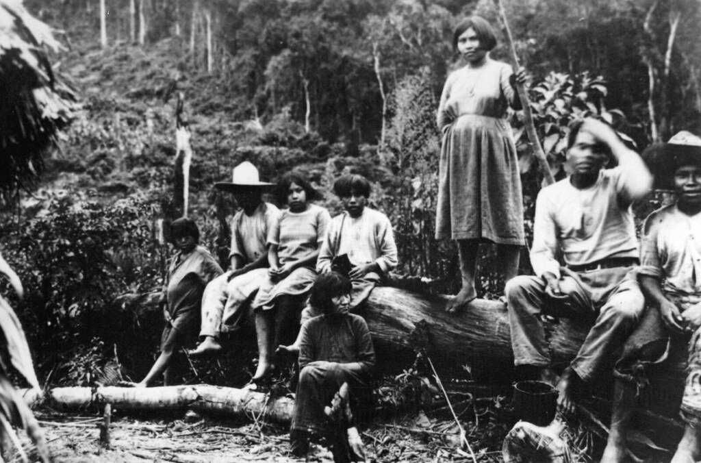 Indígenas sentados em pedaço de madeira