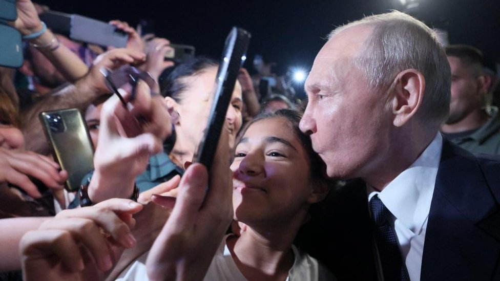 Russian President Vladimir Putin kisses a woman's head surrounded by people in Derbent in the southern region of Dagestan, Russia, June 28, 2023.
