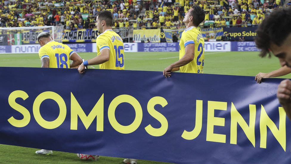 Cadiz players with a sign saying "we are Jenni" ahead of their match against UD Almeria