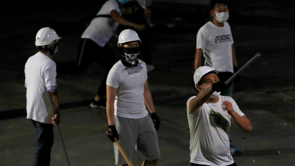 Мужчины в белых футболках с шестами видны в Юэнь Луне после нападения на демонстрантов, выступающих против экстрадиции, на вокзале в Гонконге