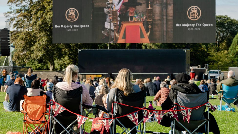 Pessoas assistem à cerimônia em telão instalado no Holyrood Park, em Edimburgo, capital da Escócia