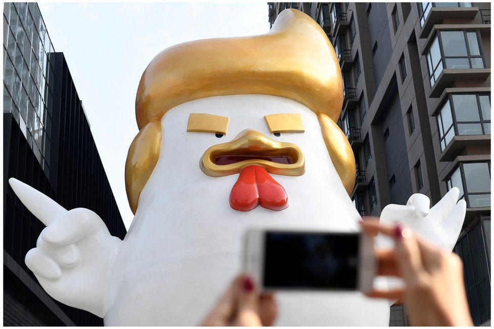 Гигантская скульптура петуха, напоминающая Дональда Трампа, возле торгового центра в Тайюане, провинция Шаньси, с мобильным телефоном, который держит женщина за руки на переднем плане. 24 декабря 2016 г.