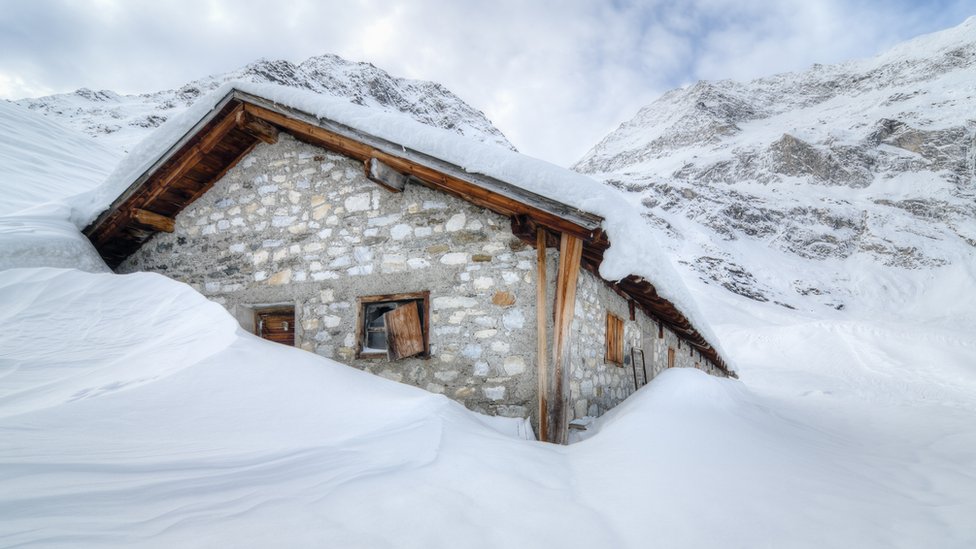 Una cabaña rodeada y cubierta de nieve