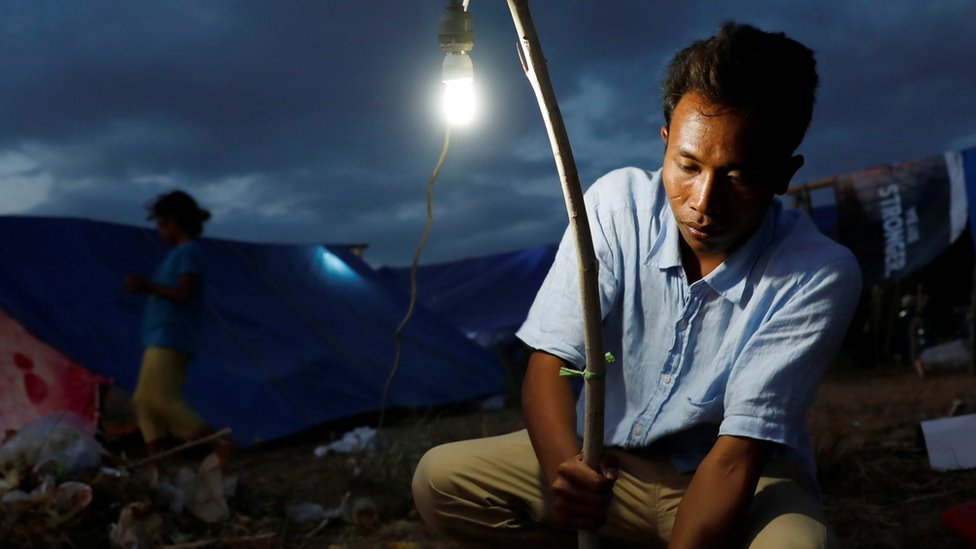 Seorang warga di Senggigi, Lombok, yang khawatir akan gempa susulan memasang lampu di depan tenda tempat mereka berlindung.