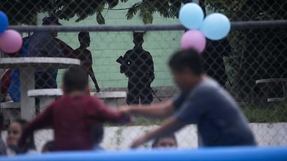 Deca se igraju na terenu, okružena naoružanim čuvarima.