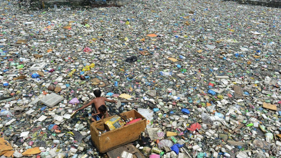 A father and son (L) on a makeshift boat made from styrofoam paddle through a garbage filled river