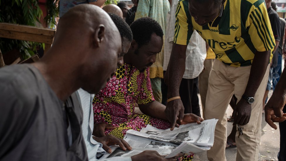 Мужчины из Нигерии изучают газету после отсрочки