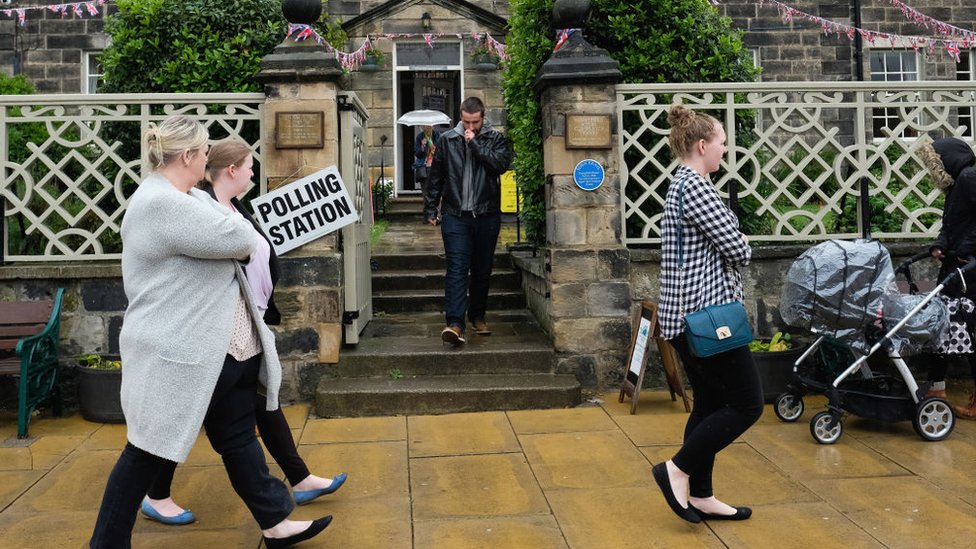 Unos 46,9 millones de personas estaban registradas para votar. Personas caminan frente a un centro de votación en Reino Unido.