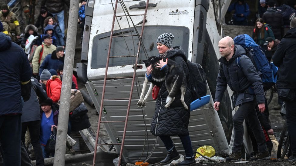 Uma mulher carrega um cachorro enquanto as pessoas atravessam uma ponte destruída na cidade de Irpin, a noroeste de Kiev, 5 de março de 2022
