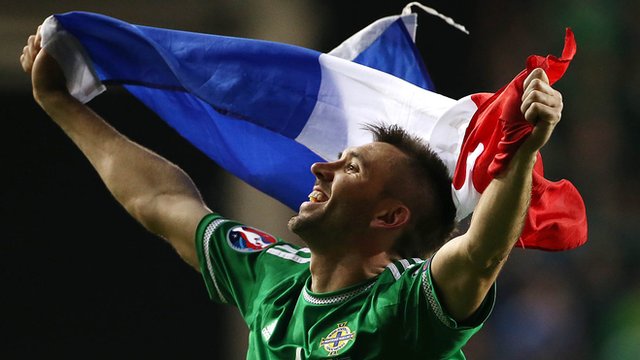 Gareth McAuley celebrates Northern Ireland's Euro 2016 qualification with the flag of finals hosts France