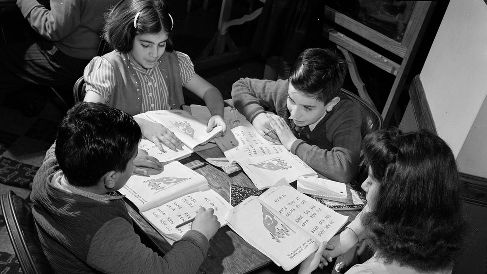 Niños turco-estadounidenses en la mesa con libros de trabajo. Niños turco-estadounidenses en la mesa con libros de trabajo.