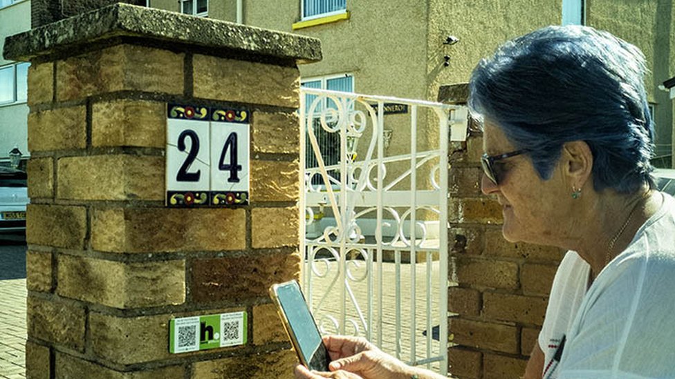 Rhyl house with woman scanning QR code of HistoryPoints.org plaque