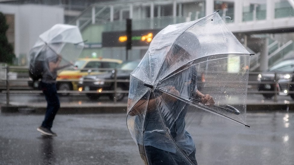 People shelter under umbrellas from the wind and rain as they cross a road near Shinjuku train station on October 12, 2019 in Tokyo, Japan