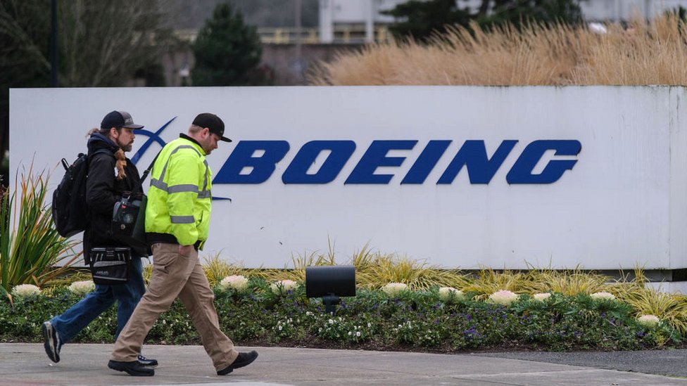 Пара рабочих проходит мимо вывески Boeing