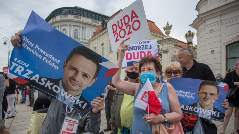 Сторонники президента Анджея Дуды и его соперника мэра Варшавы Рафала Трзасковски держат плакаты во время предвыборной кампании по выборам президента в Варшаве, Польша, 26 июня 2020 г.