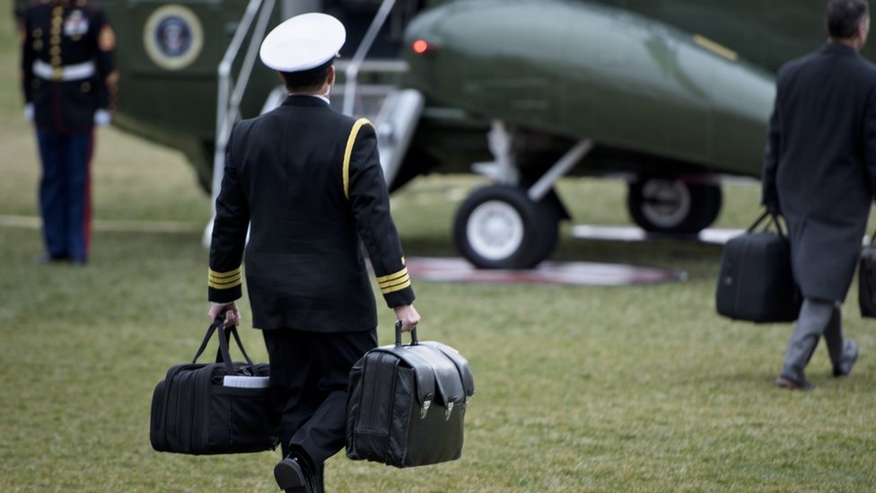 Офицер несет два портфеля к военному самолету на лужайке у Белого дома.