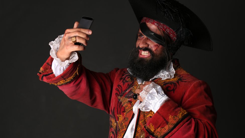 Un hombre disfrazado de pirata se mira en un teléfono.