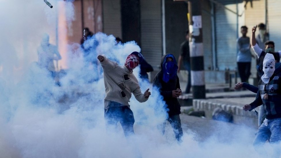 Кашмирский протестующий мусульманин в маске бросает взорвавшийся снаряд со слезоточивым газом в индийских полицейских во время акции протеста в Сринагаре, контролируемый Индией Кашмир, во вторник, 12 апреля 2016 г.